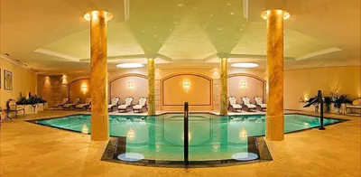 a swimming pool in a large room with chairs at Hotel Garni Dolomieu in Selva di Val Gardena