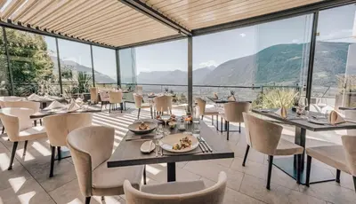 a restaurant with tables and chairs and a view of mountains at Panoramahotel Am Sonnenhang in Tirolo