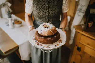 a woman holding a plate with a chocolate cake on it at Bäcksteinerhof in Merano