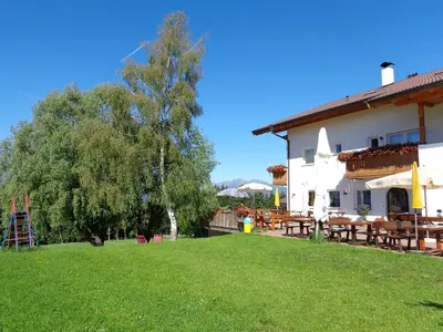 a building with a yard with wooden tables and a tree at Gasthof St. Ulrich in Meltina
