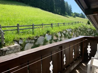 a stone retaining wall with a fence and a field at Apartments La Vara in Corvara in Badia