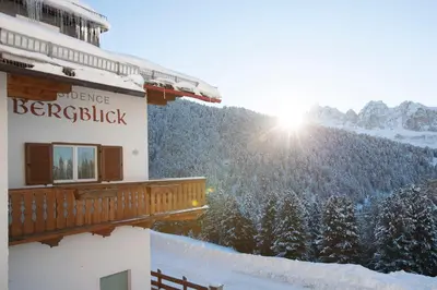 a building with the sun shining on a snow covered mountain at Residence Bergblick in Bressanone