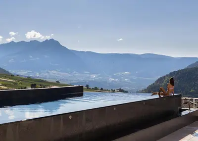 a woman sitting on a wall next to a body of water at Alpin & Stylehotel Die Sonne in Parcines
