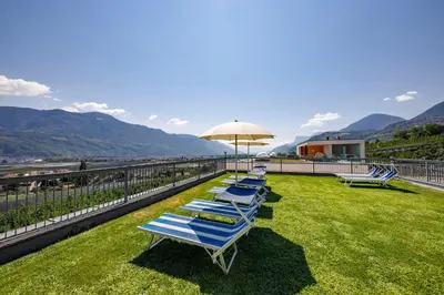 a row of lounge chairs and an umbrella on a lawn at Ferienhaus Törggelehof in Cermes