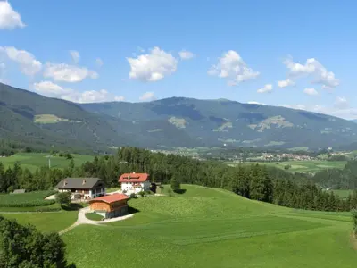 a house on a green hill with mountains in the background at Zangerlechnhof in Brunico