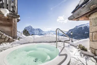 a hot tub in the snow with mountains in the background at Almhotel Col Raiser in Santa Cristina in Val Gardena