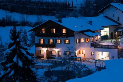 a house with lights on in the snow at night at Peternaderhof in Vols am Schlern
