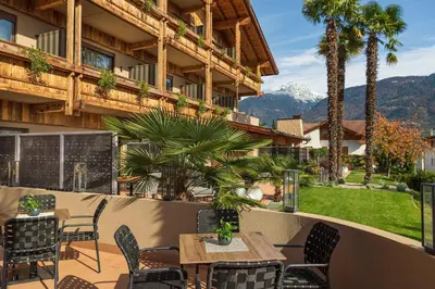 a patio with a table and chairs and mountains at MONDI Hotel Tscherms in Cermes
