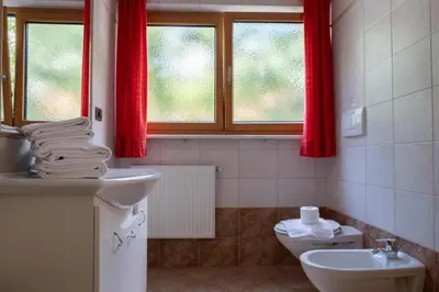 a bathroom with a sink and a toilet and red curtains at Ferienwohnung im Haus Texel II in Parcines