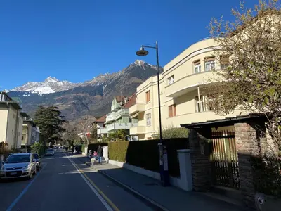 a street with a building and mountains in the background at Delightful Villa Rina in Merano