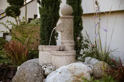 a stone fountain sitting on a rock in a garden at Apartments ANNY in Postal