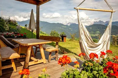 a wooden deck with a hammock and a table and flowers at Oberhauser Hof - Apartments in Feldthurns