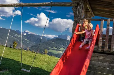 two children playing on a slide in a playground at Oberhauser Hof - Apartments in Feldthurns