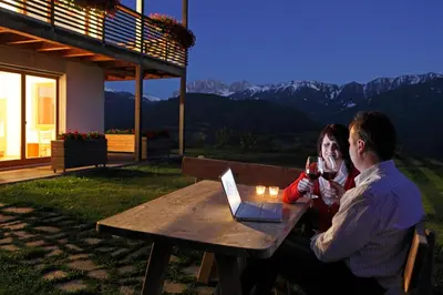 a man and woman sitting at a picnic table with wine glasses at Oberhauser Hof - Apartments in Feldthurns