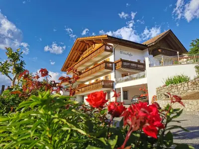 a building with red flowers in front of it at Pension-Appartement Mitterhofer in Schenna