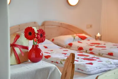 a red vase with flowers on a table with two beds at Ebenhof in Collepietra