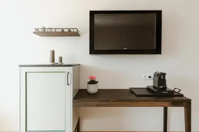 a desk with a tv on a white wall with a table with a table at Ansitz am Eck by Hotel Pernhof in Termeno