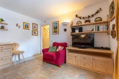 a living room with a red chair and a flat screen tv at Casa Rosi in Pozza di Fassa
