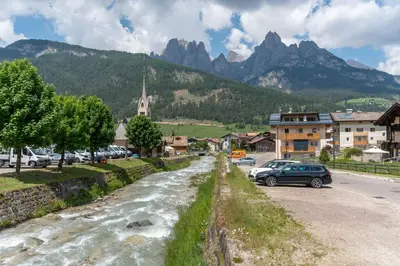 a street in a town with cars parked next to a river at Casa Rosi in Pozza di Fassa