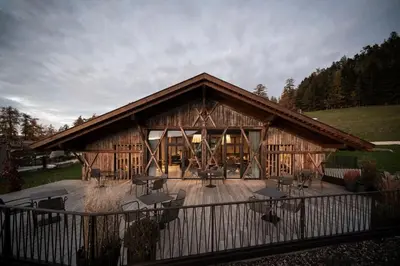 a large wooden cabin with tables and chairs on a deck at Gfell in Vols am Schlern