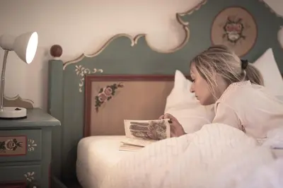 a woman laying in bed reading a book at Village Charme in Molini di Tures