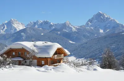 a log cabin covered in snow with mountains in the background at Tiefentalhof - Urlaub am Bauernhof in Tesido