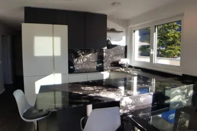 a kitchen with a black counter top with two chairs at Gardenpark Loft in Ora/Auer
