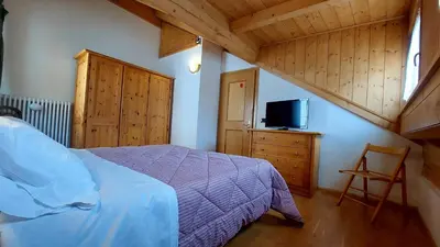a bedroom with a bed and a tv and wooden ceilings at Appartamento Fiocco Di Neve in Campitello di Fassa