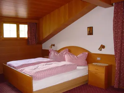 a bedroom with a wooden bed with pink pillows at Garnì Conturina in Santa Cristina in Val Gardena
