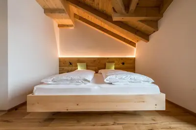 a bedroom with a wooden bed with white sheets and pillows at Rauchenbichlerhof in Brunico
