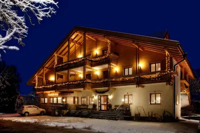 a large wooden house with a balcony at night at Pension Panorama in Monguelfo