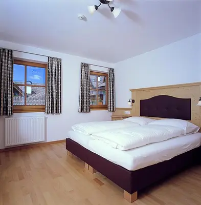 a bedroom with a large bed and two windows at Apartments Rusctlea in Selva di Val Gardena