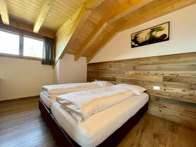 two beds in a room with a wooden wall at Sartu Apartments in San Vigilio Di Marebbe