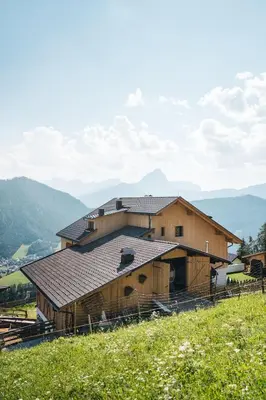 a large wooden barn with mountains in the background at Sartu Apartments in San Vigilio Di Marebbe