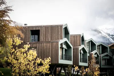 a building with wooden facade with mountains in the background at Floris Green Suites by Parc Hotel Florian in Siusi