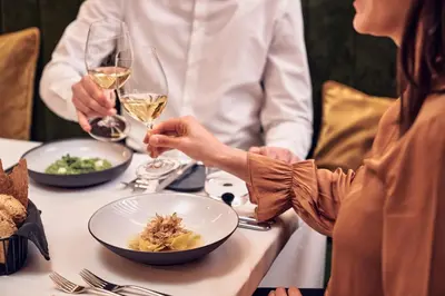 two people sitting at a table with a bowl of food and wine at Falkensteiner Hotel Kronplatz - The Leading Hotels of the World in Brunico