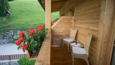 a wooden staircase with two chairs and a vase with red flowers at Holzerhof in Valdaora di Sotto