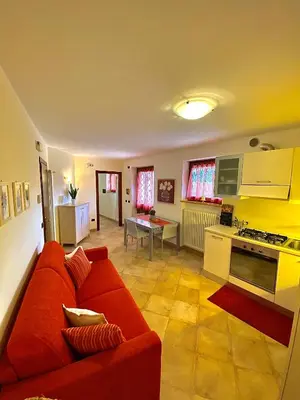 a living room with a red couch and a kitchen at Appartamento Le Colonne - Relais Villa Quercia in Tassullo