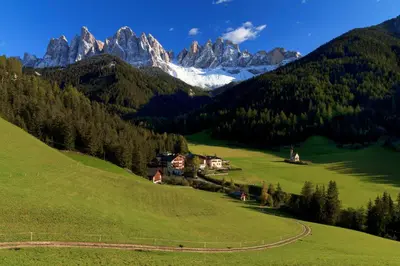 a house on a green hill with mountains in the background at Hotel Ranuimüllerhof in Villnoss
