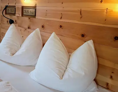 a bed with white pillows on it with a wooden wall at Koflhof Urlaub auf dem Bauernhof in Aldino
