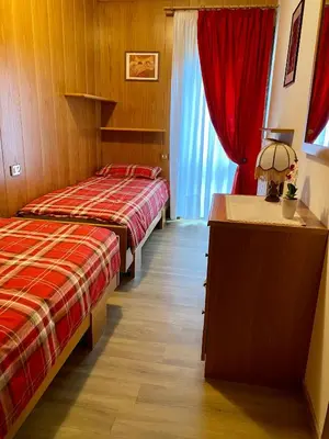 two beds in a hotel room with red curtains at Villa Tisot in Fiera di Primiero