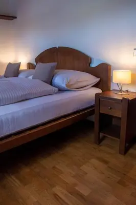 a bed with a wooden headboard and a table with a lamp at Apartments Ciasa Colz in La Villa