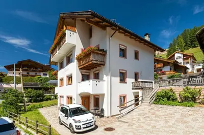 a white house with a car parked in front at Apartments Puntin in San Cassiano