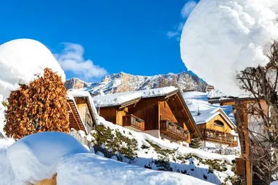 a log cabin in the snow with mountains in the background at Ciasa Odlana in San Cassiano