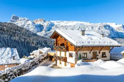 a house covered in snow with mountains in the background at Ciasa Odlana in San Cassiano
