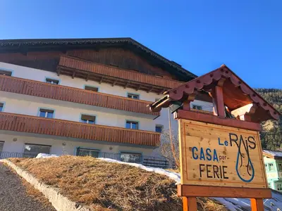 a wooden sign in front of a building at Casa per Ferie Le Rais in Pozza di Fassa