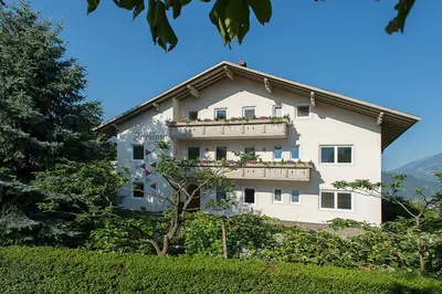 a white building with a balcony with flowers on it at Pension Etschland in Tirolo