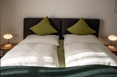 a bed with white sheets and green pillows at Puenlandhof in Brunico