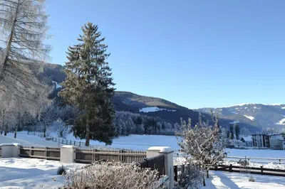 a fence in the snow with a lake and mountains at Apartment Lukas Huber in Brunico