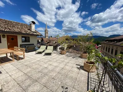 a patio with a table and benches and a church at Goldengel Ferienwohnung im Herzen Kalterns mit einer Terasse zum verlieben in Caldaro